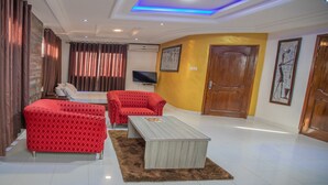 Habitación de hotel con diseño moderno, que incluye una cama grande, dos sofás rojos, una mesa de centro de madera y un televisor de pantalla plana.