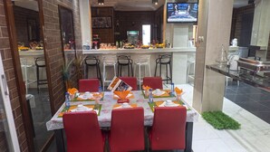 Un restaurante con pared de ladrillo, una pantalla de televisión y una mesa dispuesta para seis personas con sillas rojas.