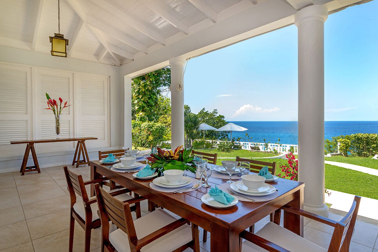 A dining area with a table set for six, overlooking a scenic view of the ocean.