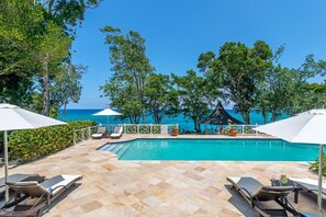 A poolside area with lounge chairs and umbrellas, overlooking a clear blue sea.