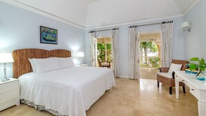 Un dormitorio con una cama grande, un escritorio y una silla. Se ve una ventana con cortinas y vistas al verde exterior.