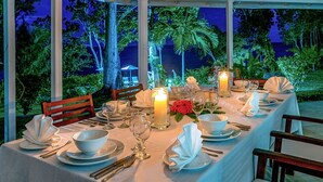 Una mesa lista para una comida, con velas, mantel blanco y vistas al exterior.