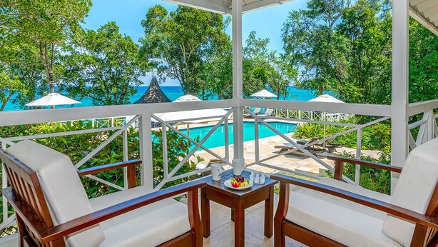 Un área de estar al aire libre techada con vista a la piscina, muebles de madera y una mesa con una bandeja de frutas.