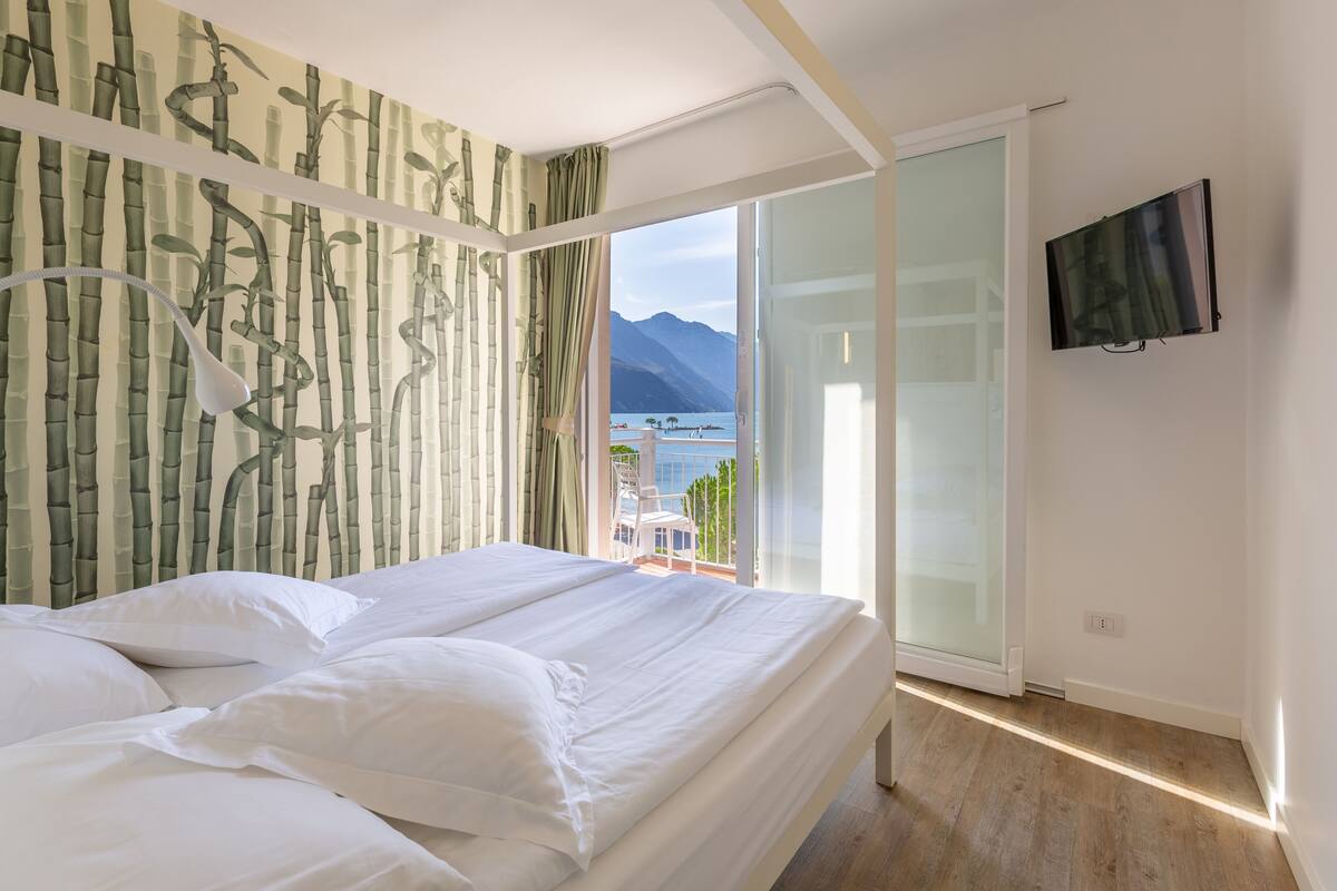 Un dormitorio con cama, televisor y vistas a la montaña y al agua.