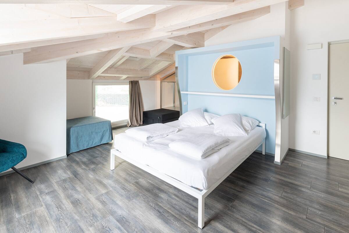 Un dormitorio moderno con cama, pared azul decorativa y un espejo circular.