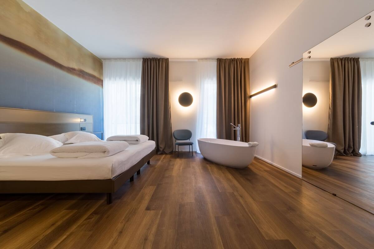 Una habitación de hotel moderna con una cama grande, una bañera, una silla y un espejo.