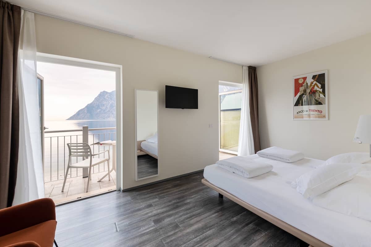 Habitación de hotel con cama, televisor, balcón con una silla y vista al mar.