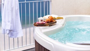 Un jacuzzi en un balcón con vistas a la montaña, una toalla colgada en la barandilla y una bandeja con aperitivos.