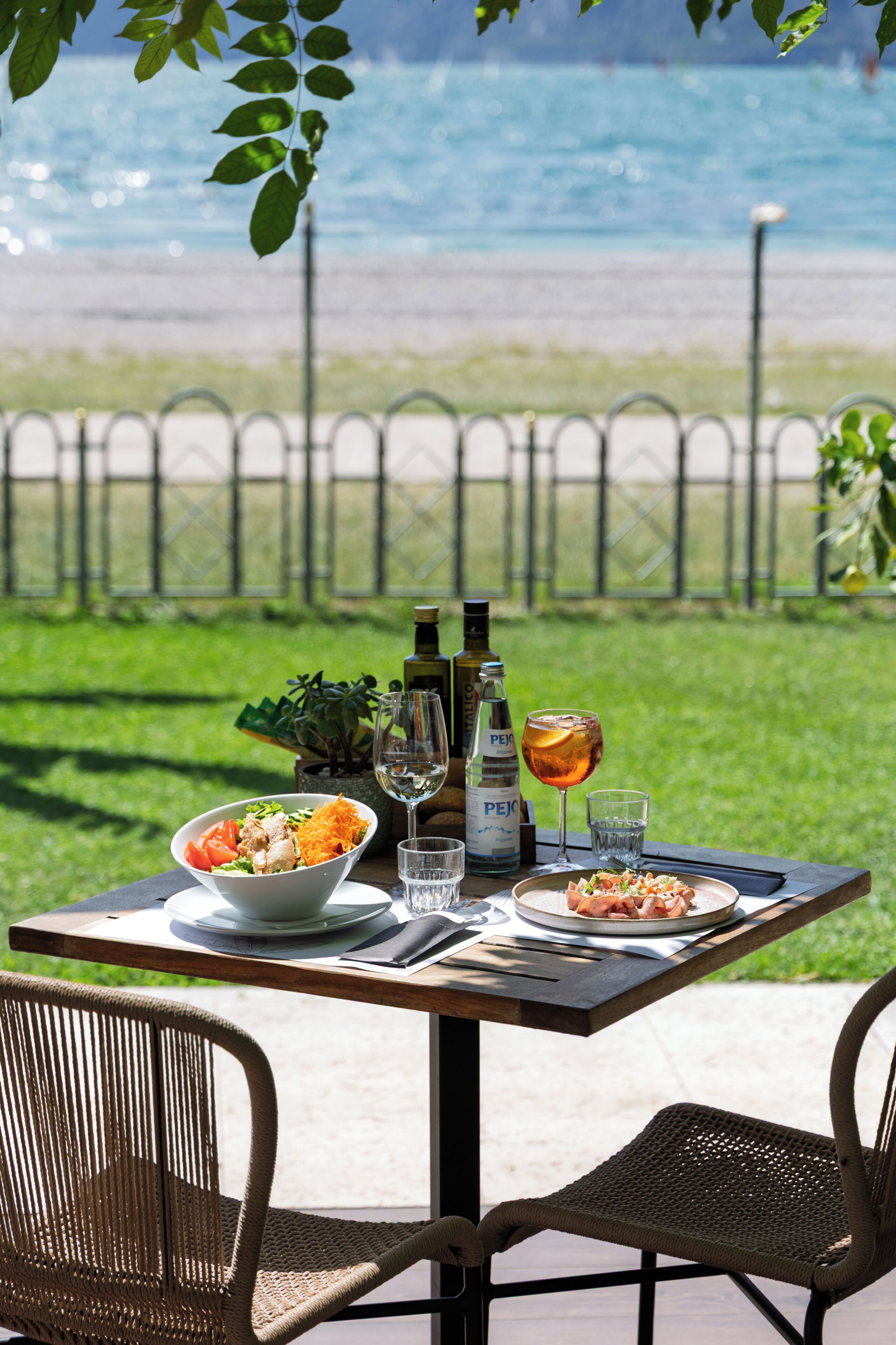 Une table à manger en plein air avec vue sur la mer, une bouteille de vin et un verre d’eau.