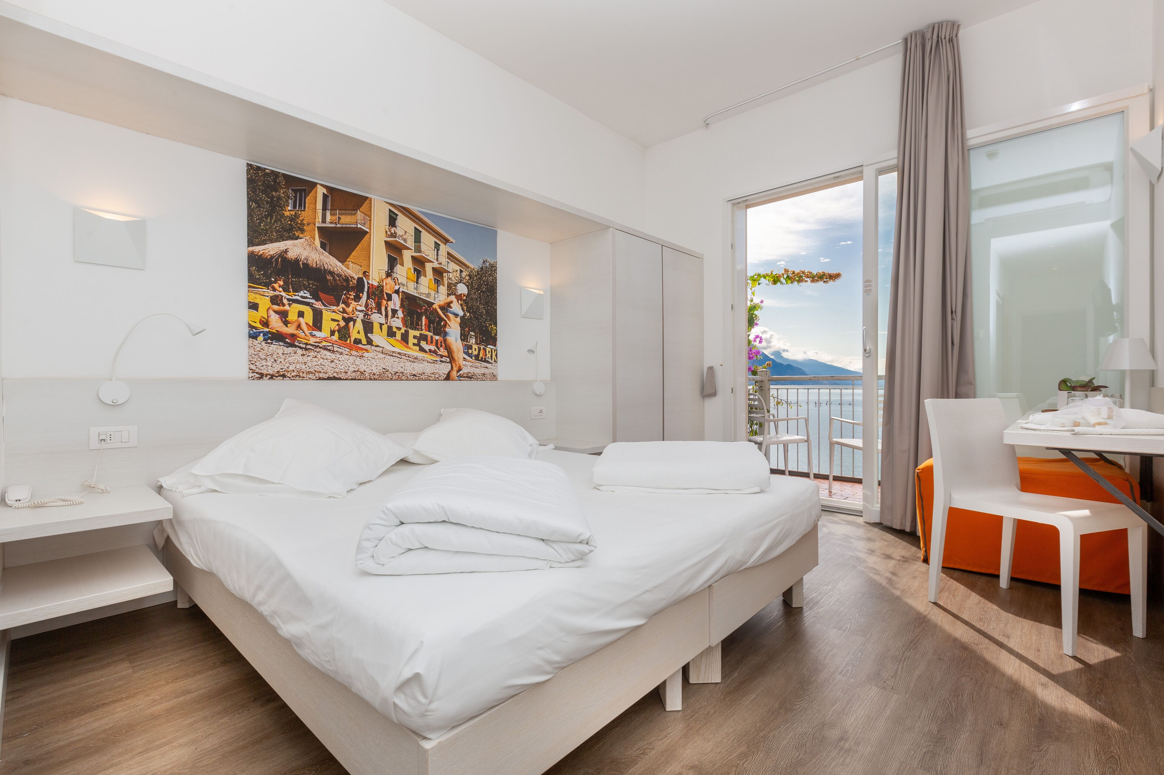 Ein modernes Hotelzimmer mit einem großen Bett, einem Schreibtisch, einem Sessel und einem Balkon mit Blick.