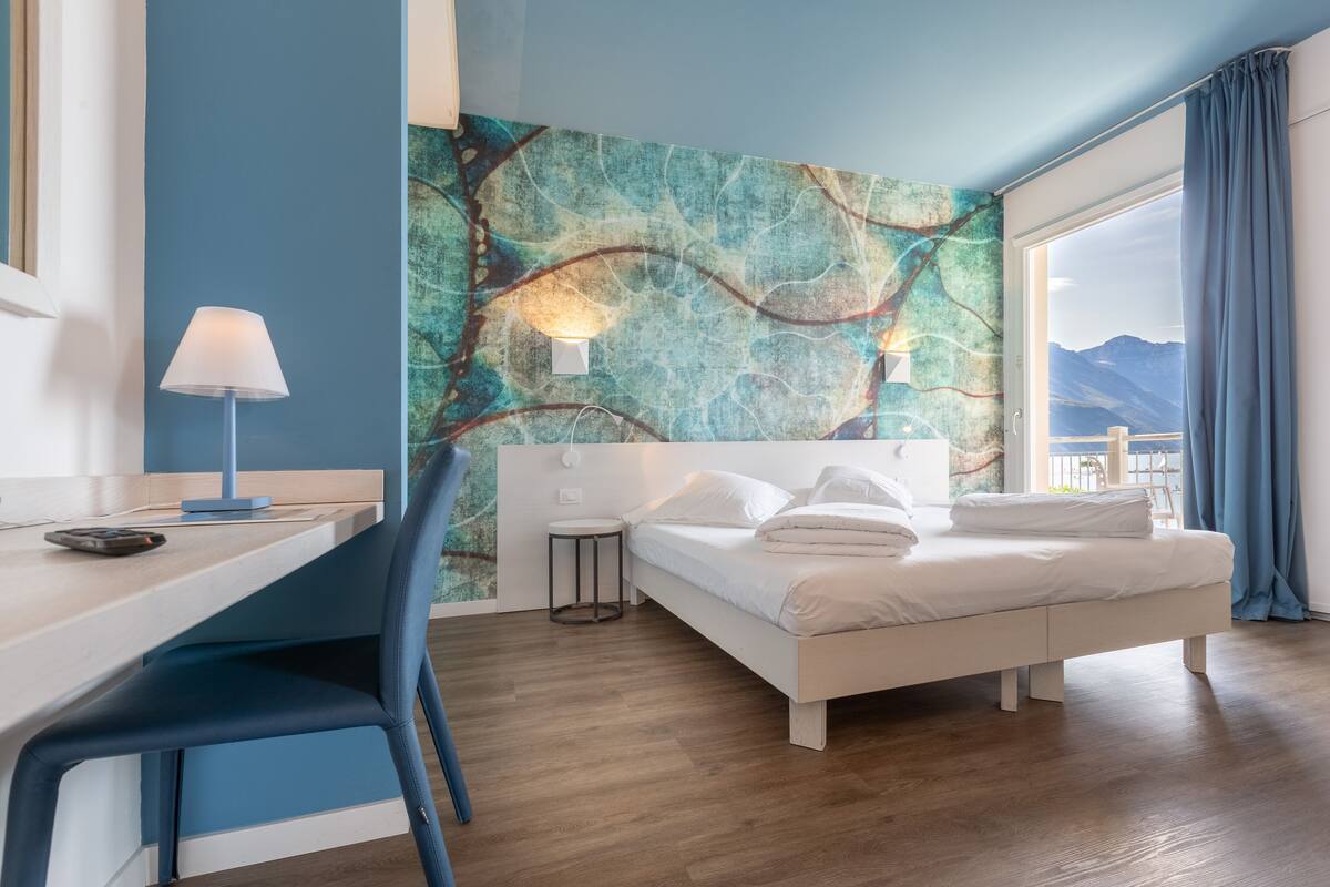 Habitación de hotel moderna con una cama, un escritorio, una silla y vistas a las montañas desde la ventana.