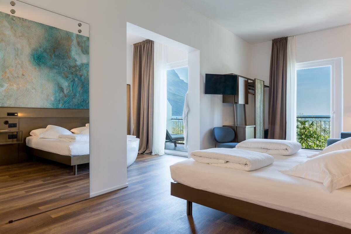 Una habitación de hotel moderna con una cama grande, televisión y balcón con vistas a las montañas.