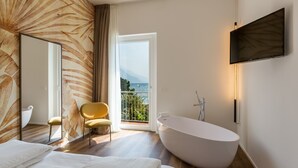 Un baño moderno con una bañera independiente, un espejo grande y vistas al mar a través de un ventanal corredero.