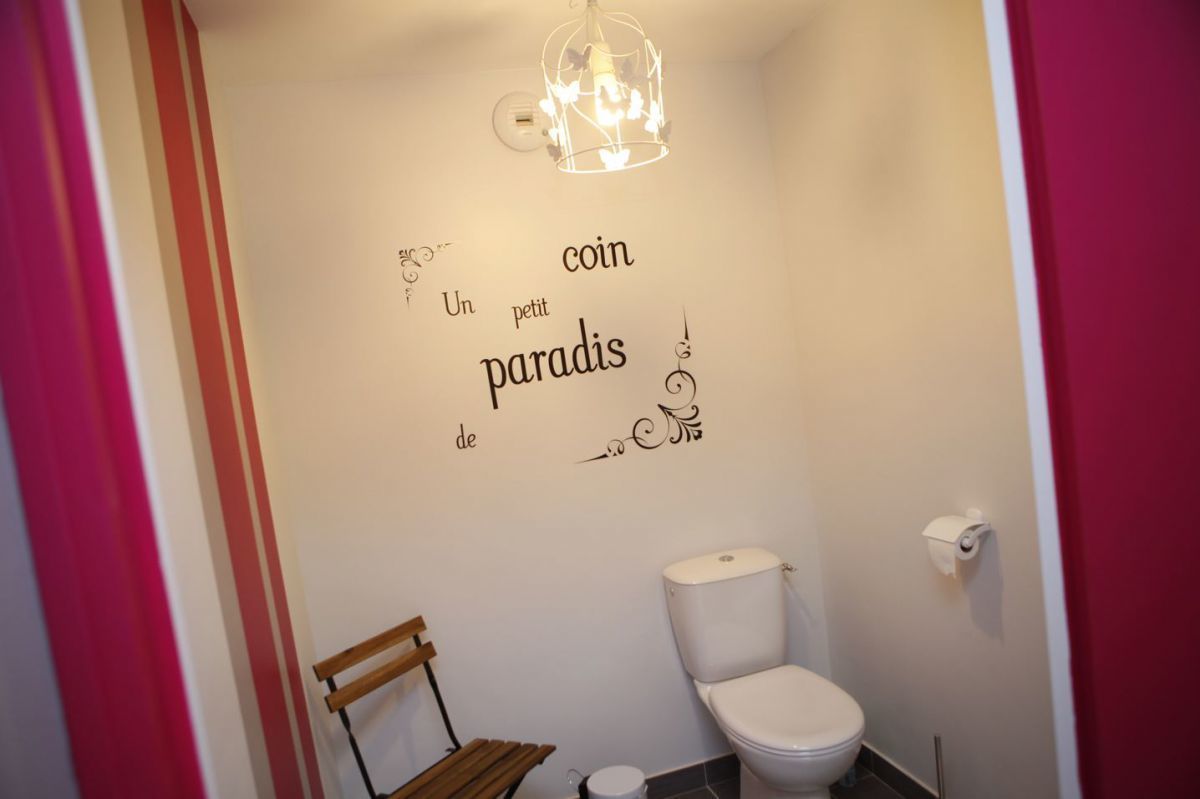 Een badkamer met een toilet, een houten stoel en een muur met decoratieve tekst.