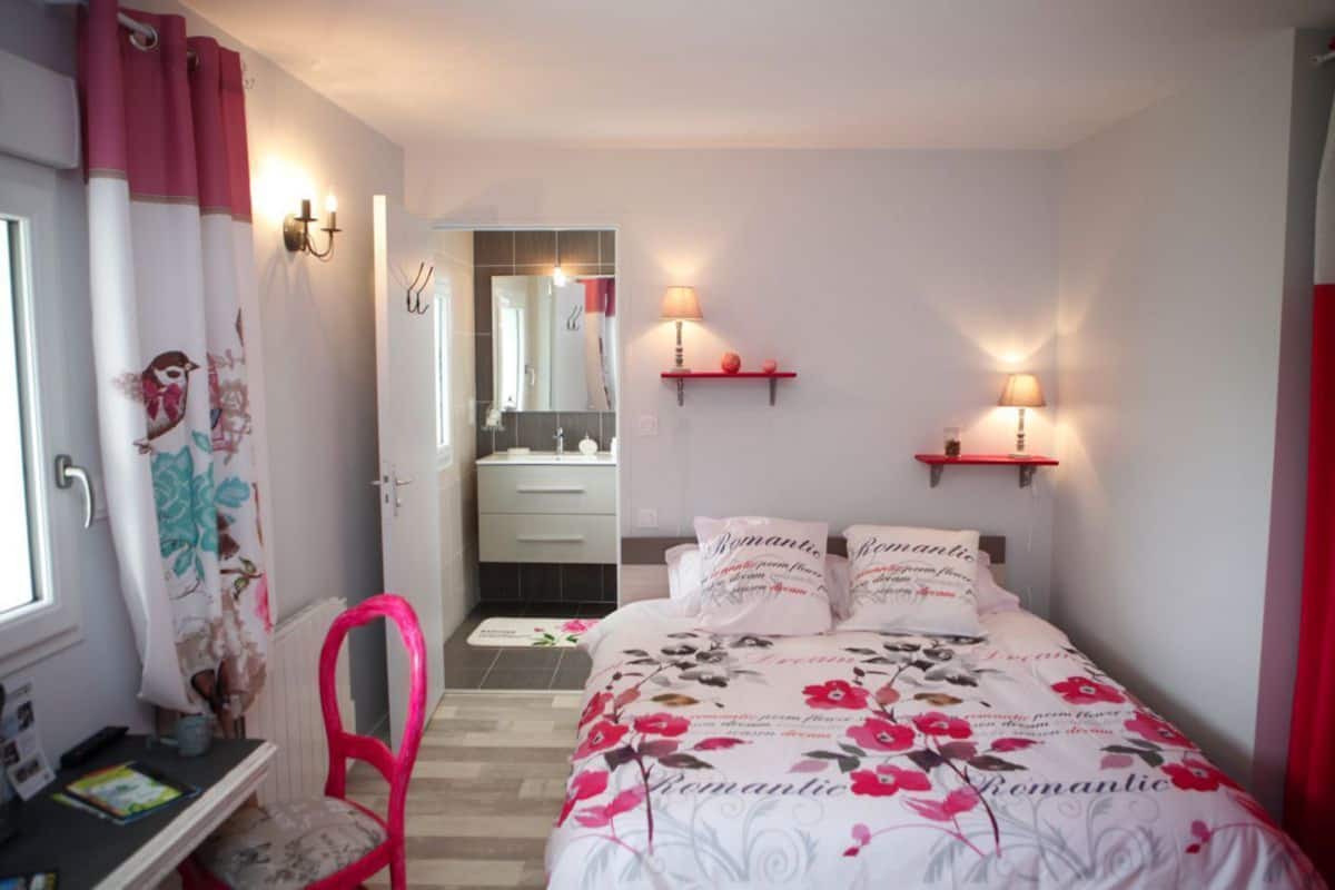 A bedroom with a bed, a chair, a desk, and a mirror.