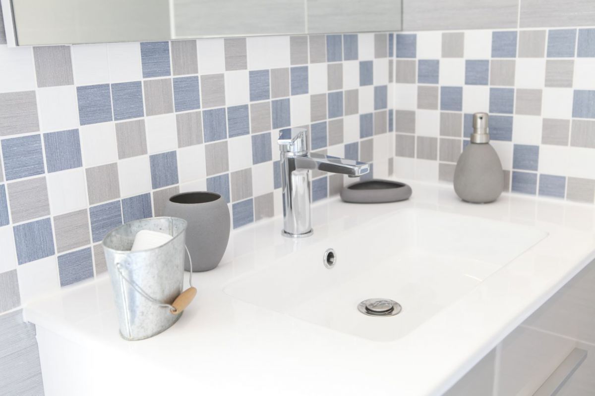 A bathroom with a white sink, a chrome faucet, a gray vase, and a metal bucket with a wooden handle.
