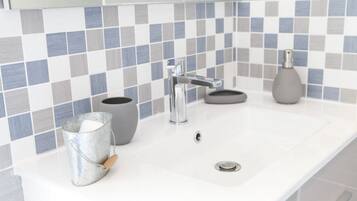 A bathroom with a white sink, a chrome faucet, a gray vase, and a metal bucket with a wooden handle.
