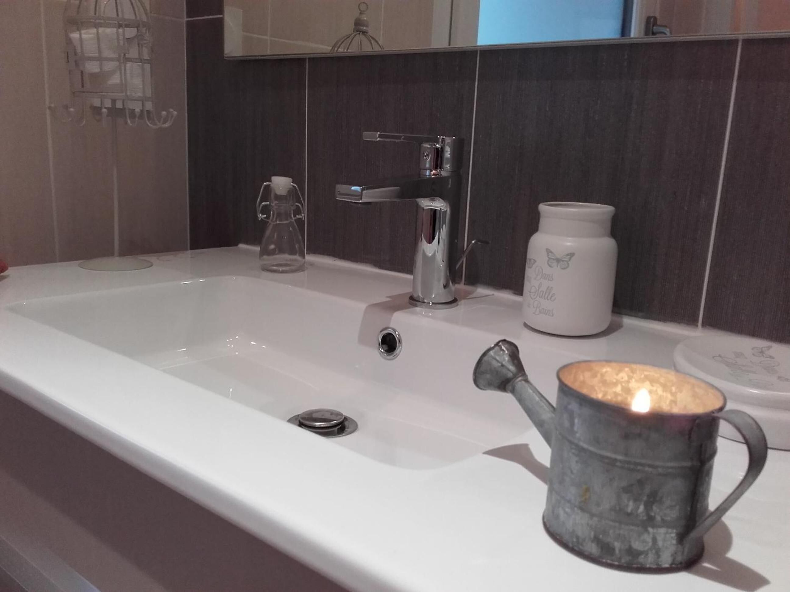 A bathroom with a white sink, a glass pitcher, a white ceramic jar, and a metal mug with a candle.