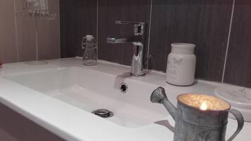 A bathroom with a white sink, a glass pitcher, a white ceramic jar, and a metal mug with a candle.