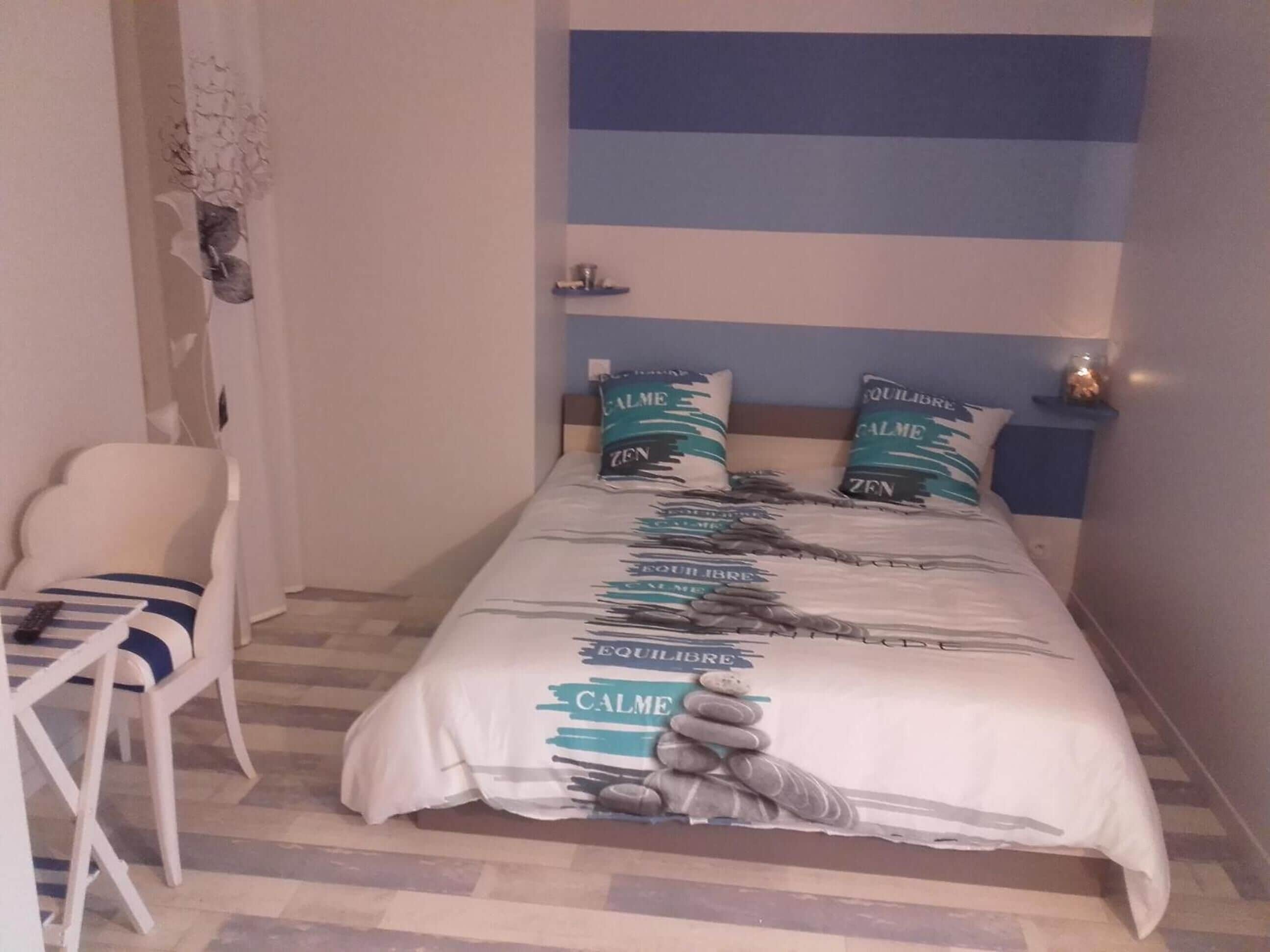 Ein Schlafzimmer mit einem Bett, zwei Kissen, einem Sessel und einem Nachttisch.