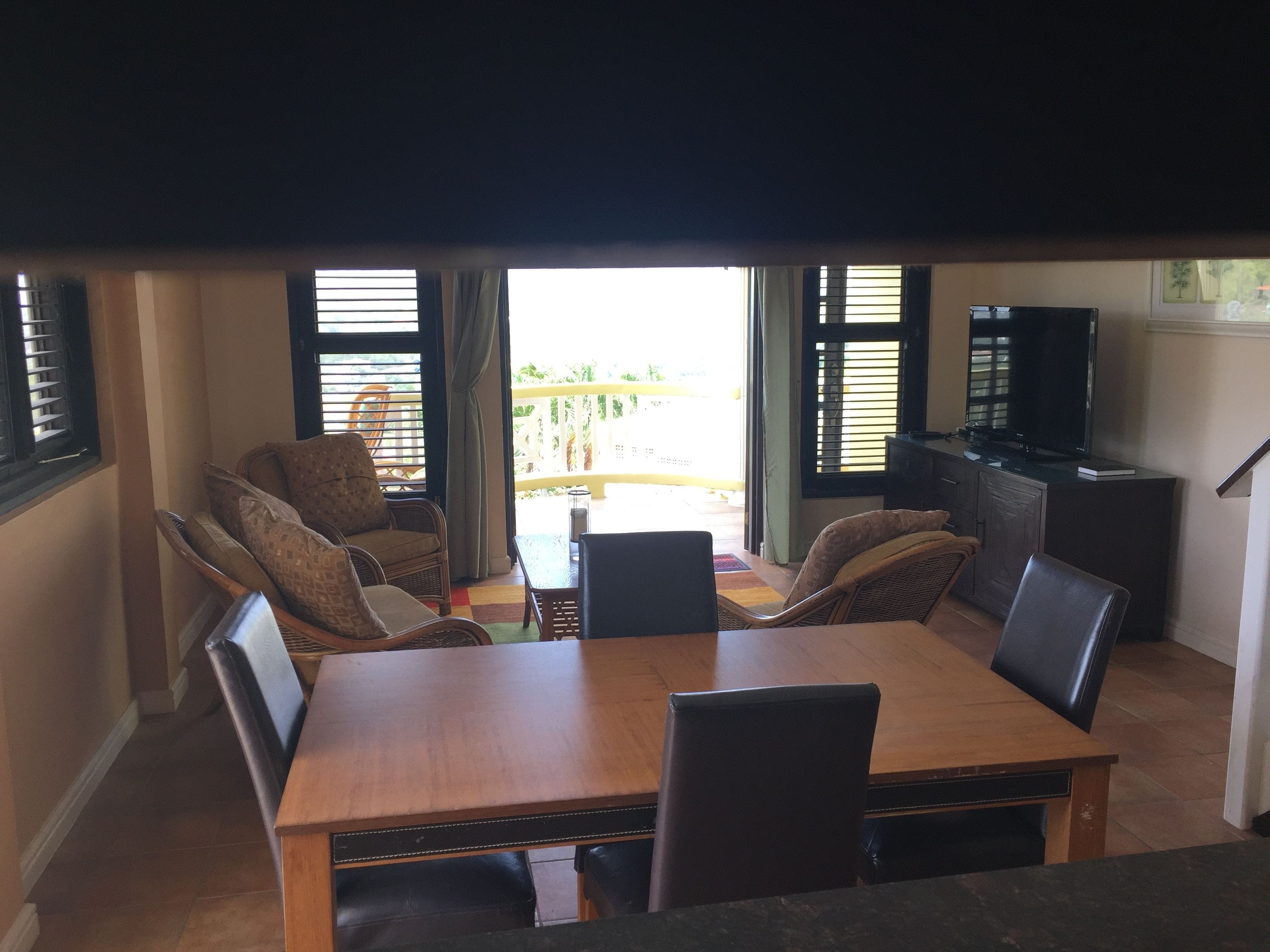 Ein Essbereich mit Holztisch und Stühlen, einem Fernseher auf einer Kommode und Blick ins Freie durch große Fenster.