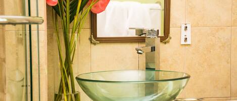 Une salle de bain avec un lavabo en forme de bol en verre, un miroir et un vase rempli de fleurs rouges.