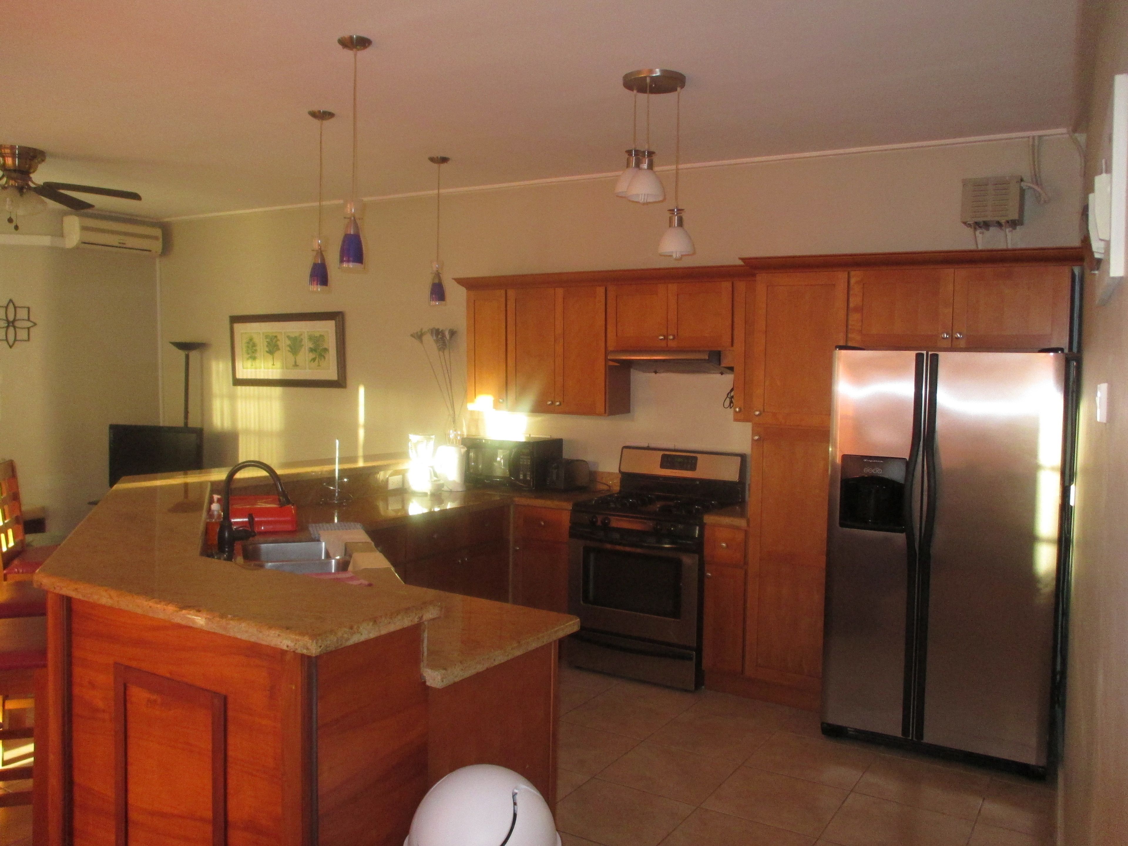 A kitchen with wooden cabinets, a stainless steel refrigerator, a stove, and pendant lights.