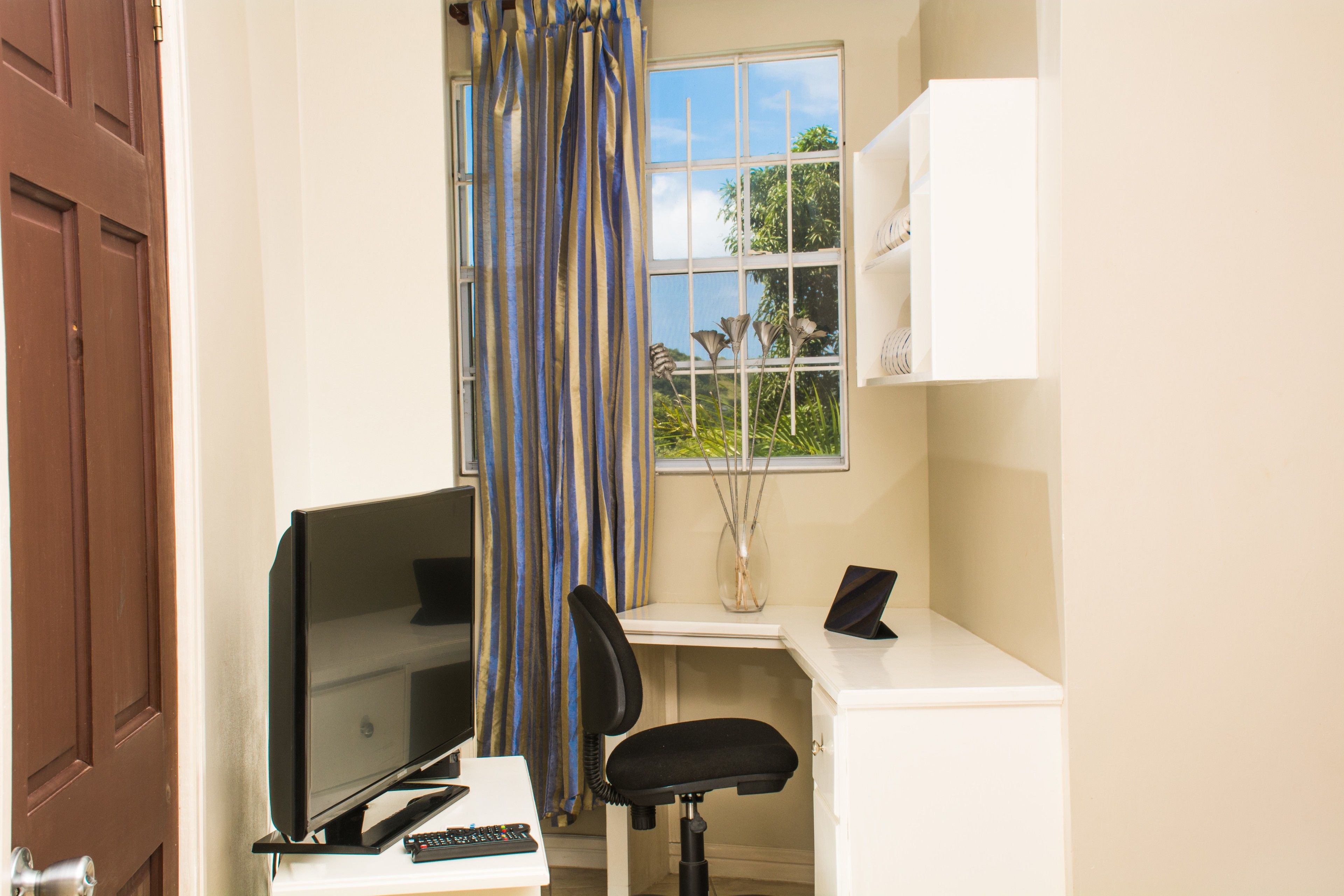 A room with a desk, chair, TV, and a window with curtains.