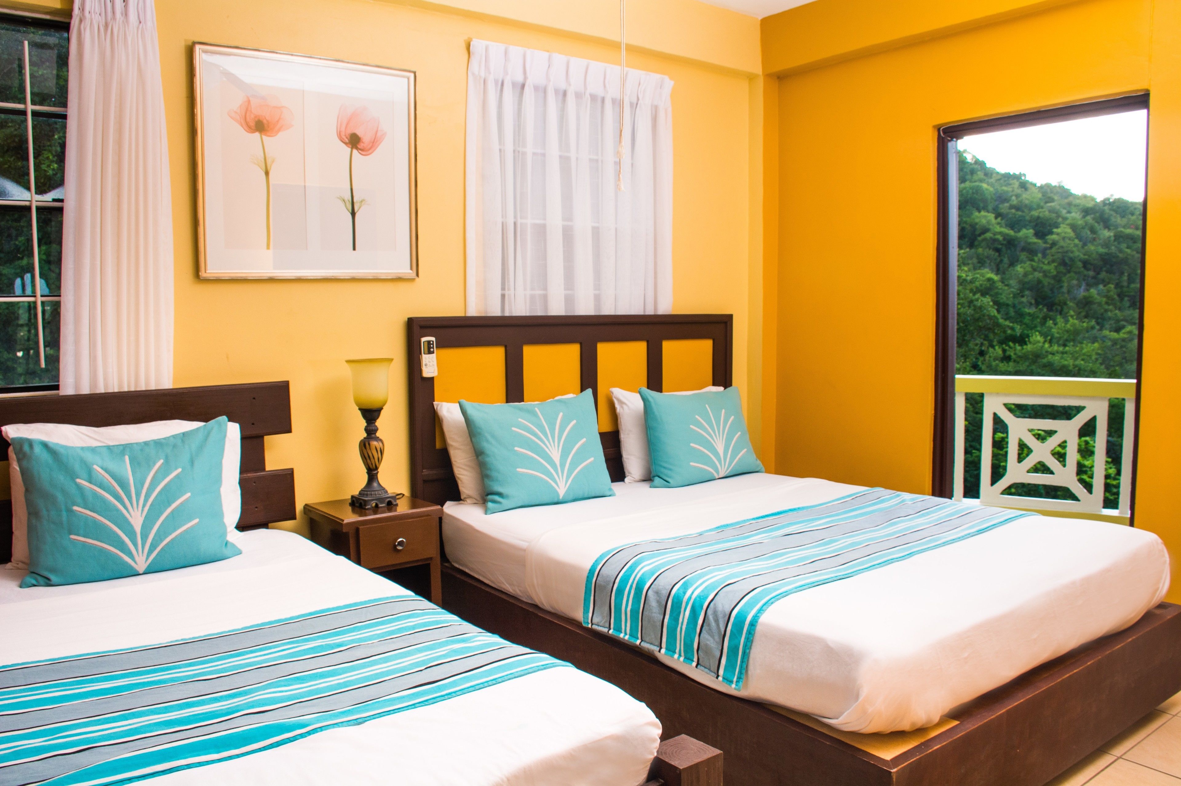 A hotel room with two beds, a window with a view of greenery, and a framed picture on the wall.
