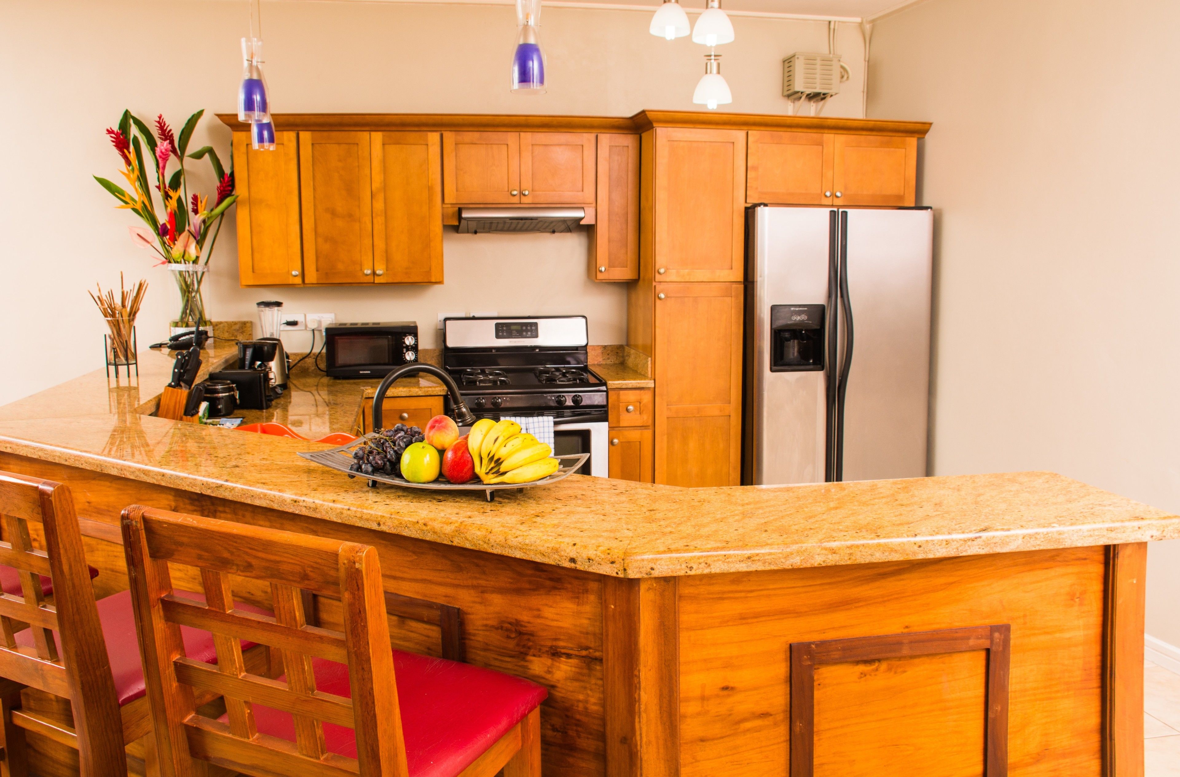 A kitchen with wooden cabinets, a stainless steel refrigerator, a stove, and a granite countertop.