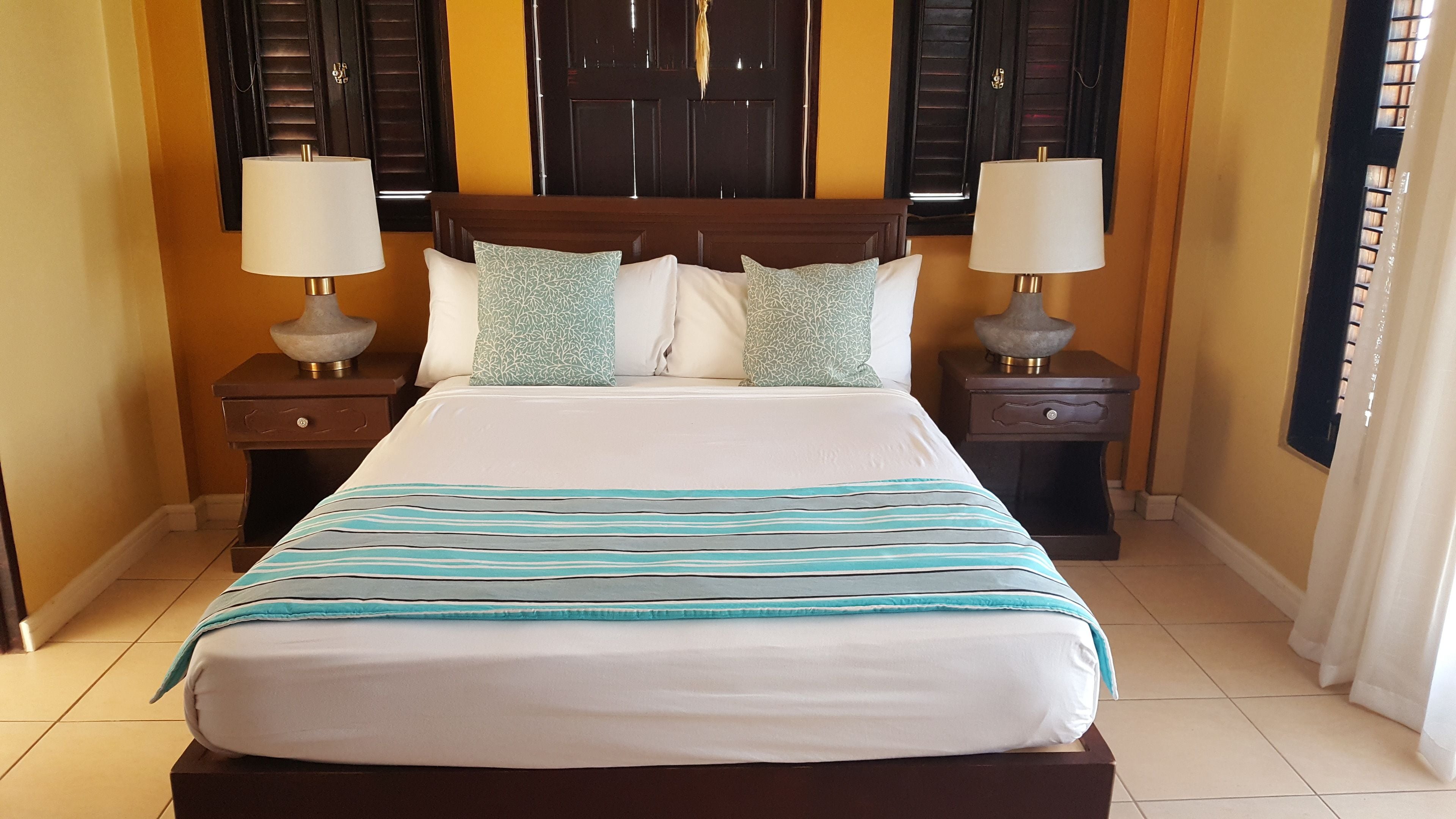 A neatly made bed with a striped bedspread, two bedside tables with lamps, and a wooden headboard.