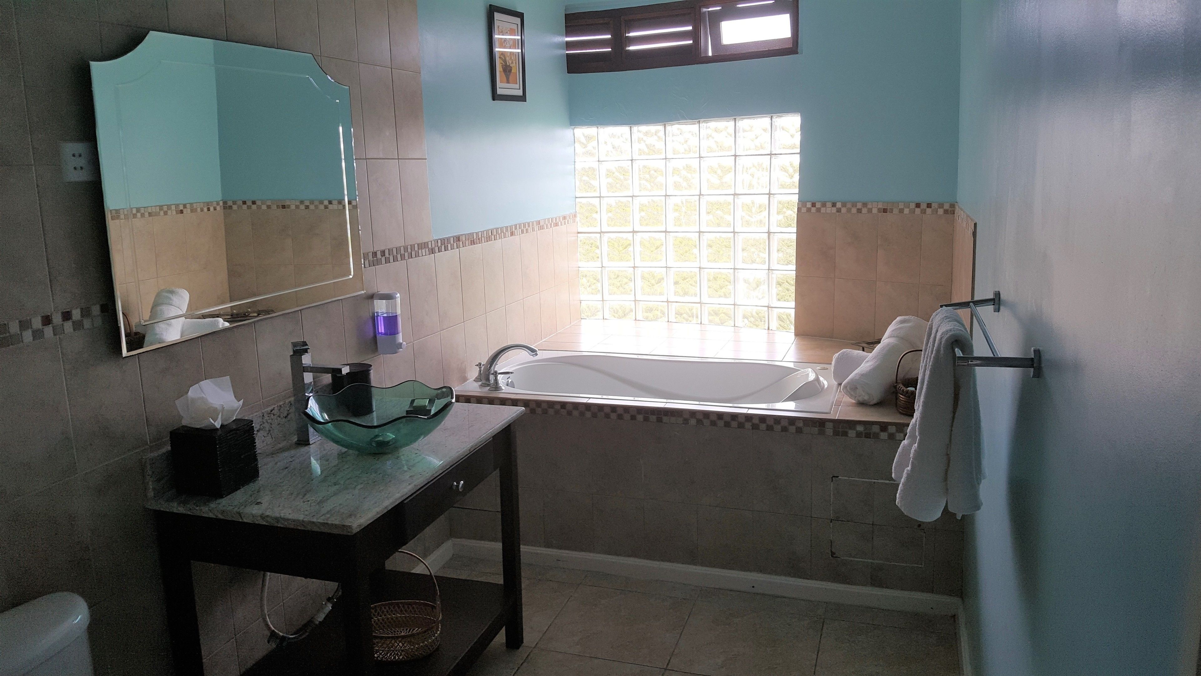 A bathroom with a glass sink, a mirror, a bathtub, and a window.