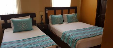Two twin beds with striped bedding, a bedside table with a lamp, and a window with curtains.