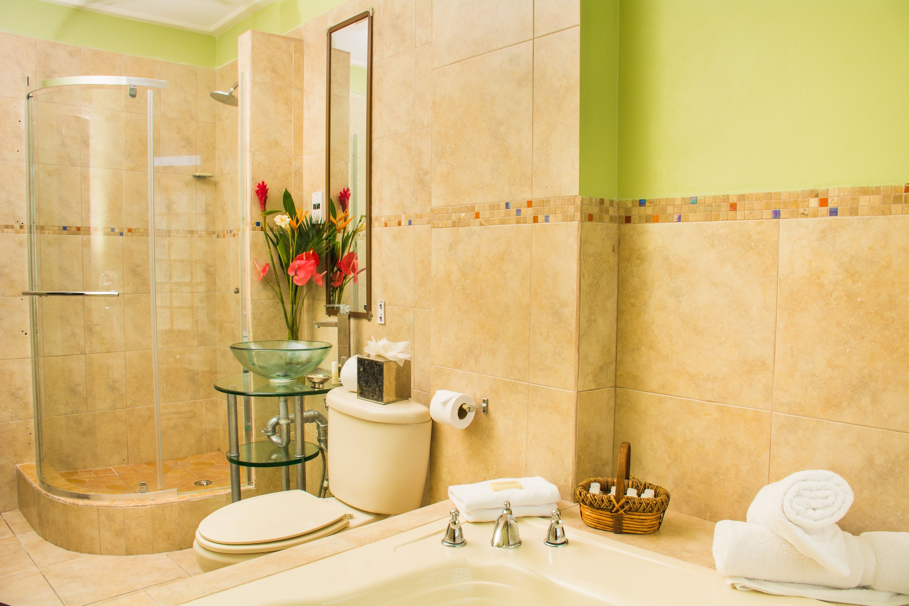 Une salle de bain avec une douche à parois de verre, des toilettes, un lavabo avec un récipient en verre, une baignoire et un miroir.