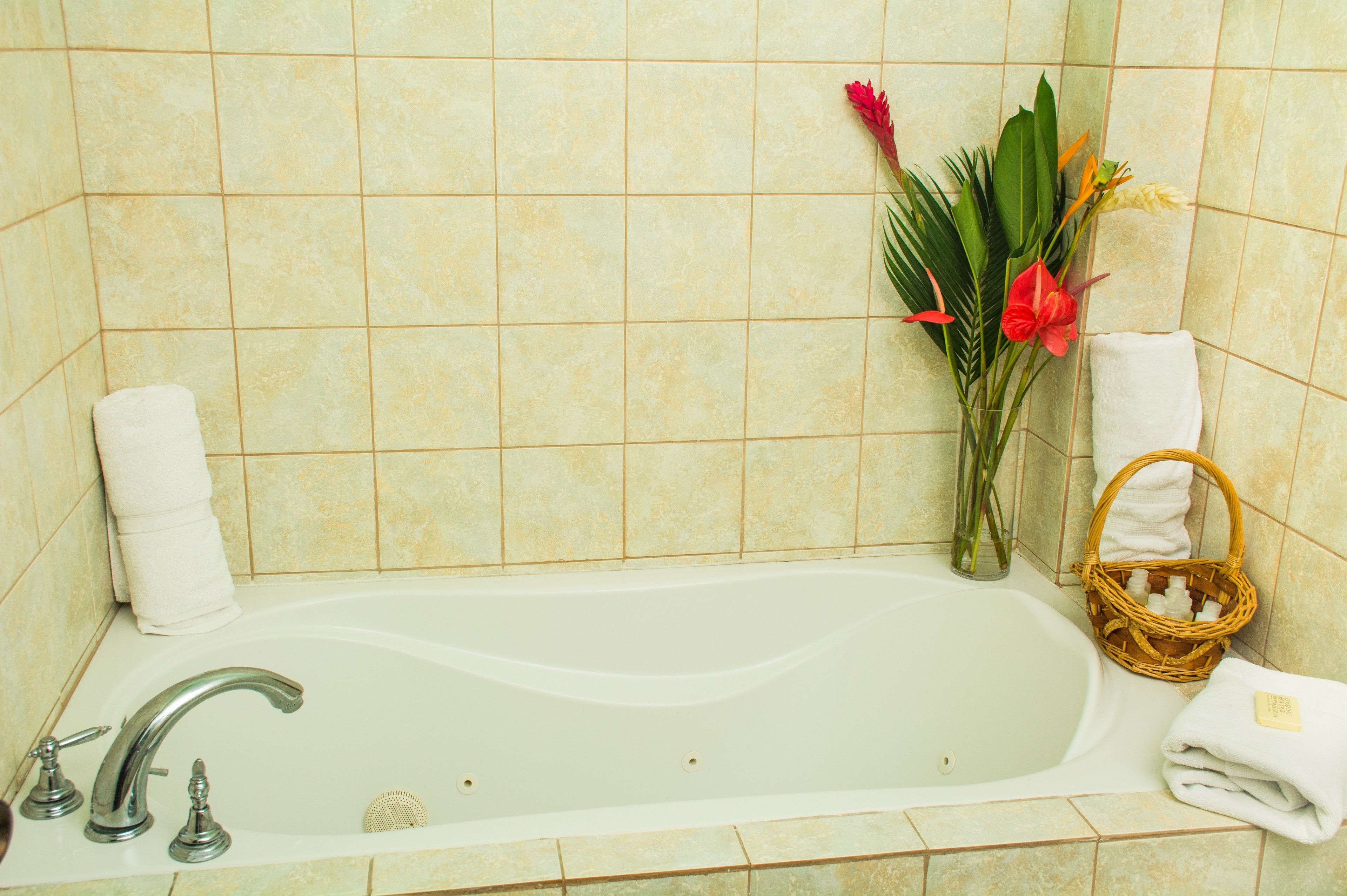 Une salle de bain avec une baignoire, une serviette blanche, un panier en osier et un bouquet de fleurs.