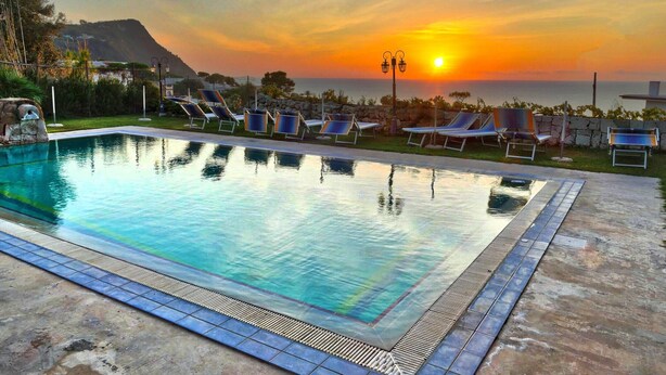 Une piscine avec des chaises longues et une vue sur le coucher de soleil.
