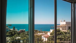 Une vue sur la côte depuis un balcon, avec un ciel dégagé, un immeuble doté d’une antenne parabolique et une vue lointaine sur la mer.