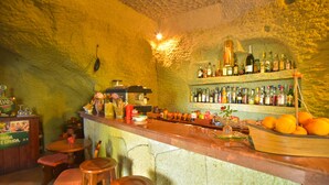 Un bar avec un mur en pierre rustique, des tabourets en bois et une variété de bouteilles et de fruits exposés sur le comptoir.