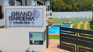 A sign for Grand Gardenia Sustainable Habitat with a view of a swimming pool and outdoor seating.
