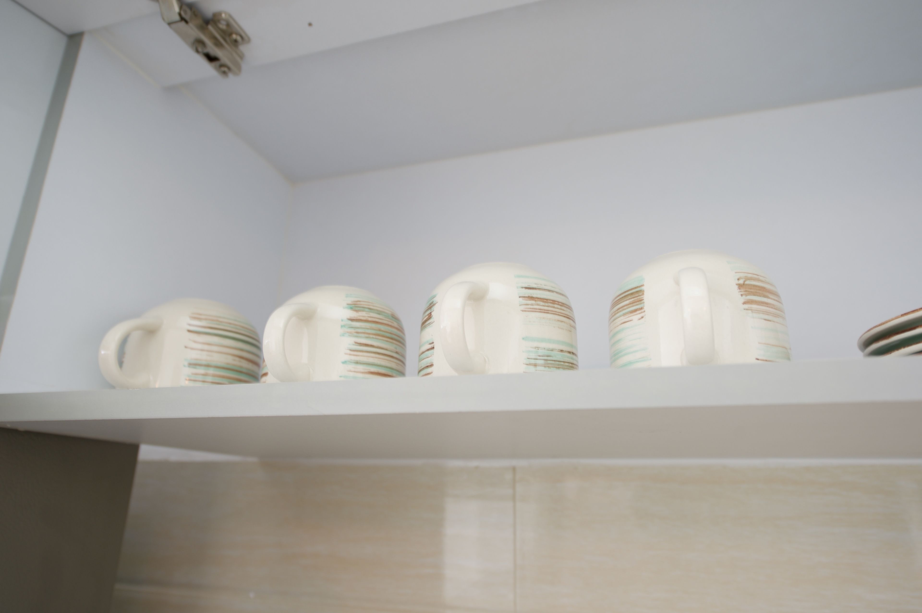A white shelf with four ceramic mugs with striped patterns.