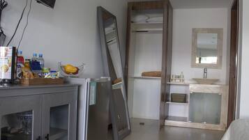 Ein Hotelzimmer mit Bett, Nachttisch mit Fernseher, Kleiderschrank, Badezimmer mit Waschbecken und Spiegel sowie einer kleinen Sitzecke mit einem Sessel.