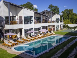 A two-story building with a swimming pool, outdoor seating, and a well-maintained lawn.