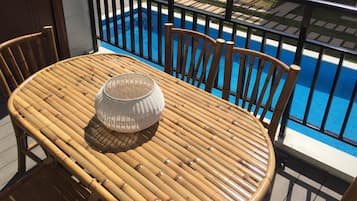 Una mesa de bambú redonda con cuatro sillas, una cesta tejida y vistas a una piscina.