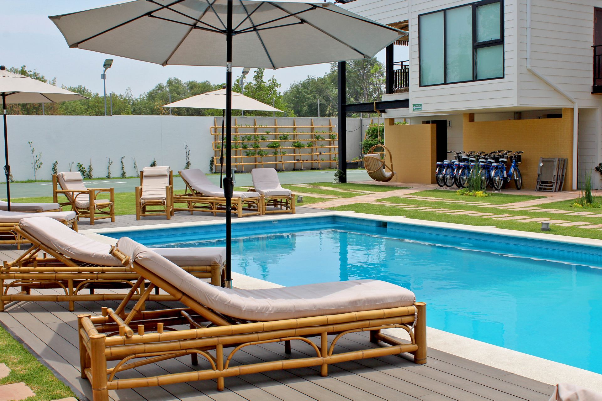 A swimming pool with lounge chairs and umbrellas, surrounded by a wooden deck and a modern building.