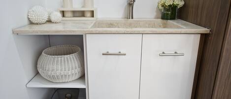 Una cocina moderna con armarios blancos, encimera de mármol, un lavabo y una cesta pequeña.