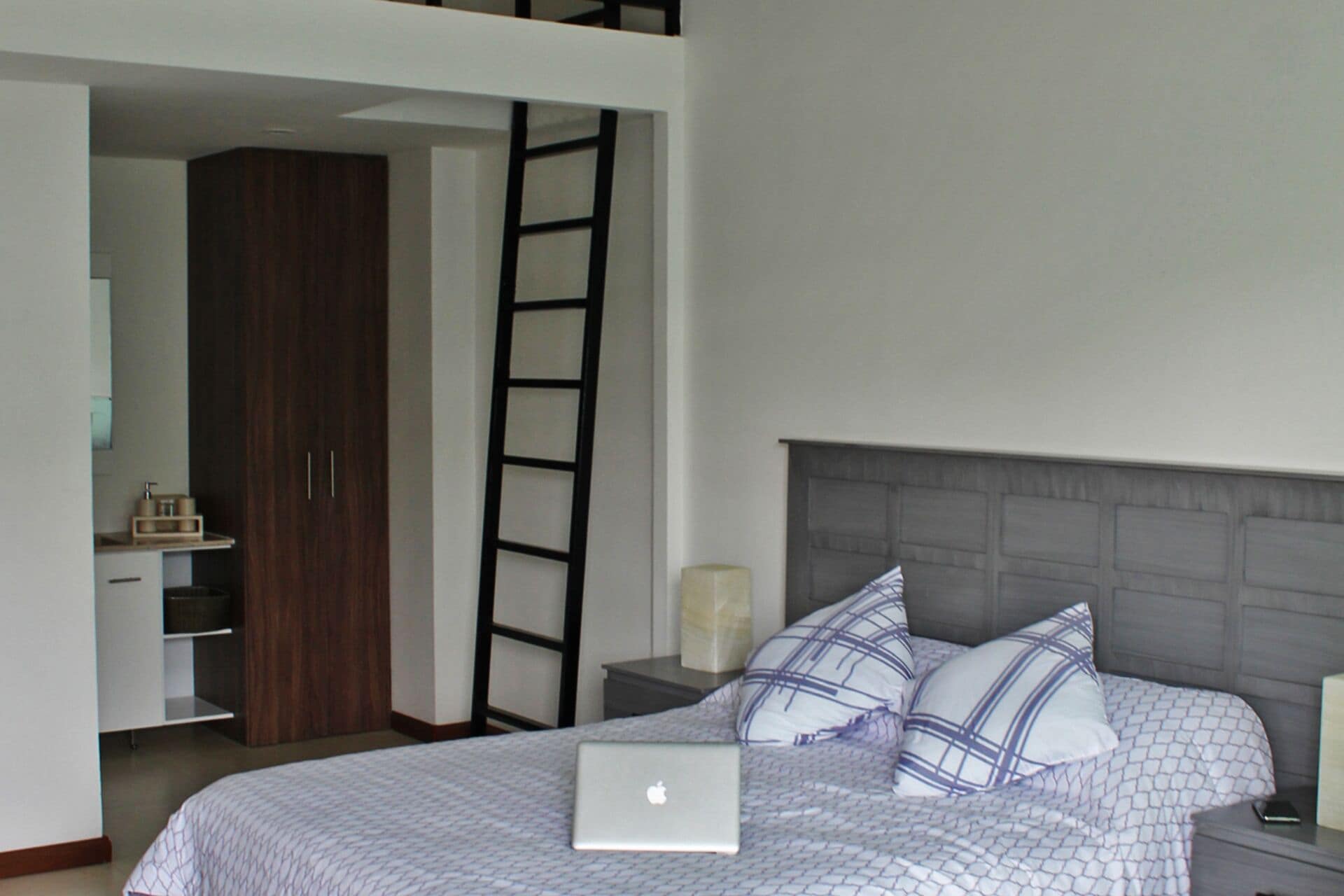 A bedroom with a bed, a laptop, a nightstand, a dresser, and a ladder.