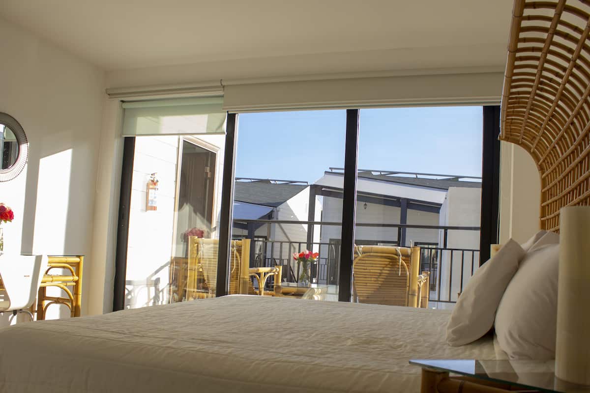Een hotelkamer met een groot bed, een balkon met rieten meubels en uitzicht op het omliggende gebouw.