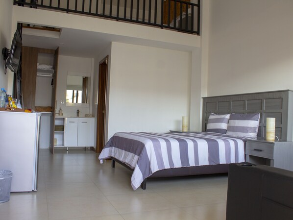 A bedroom with a bed, bedside tables, a desk, and a kitchenette.