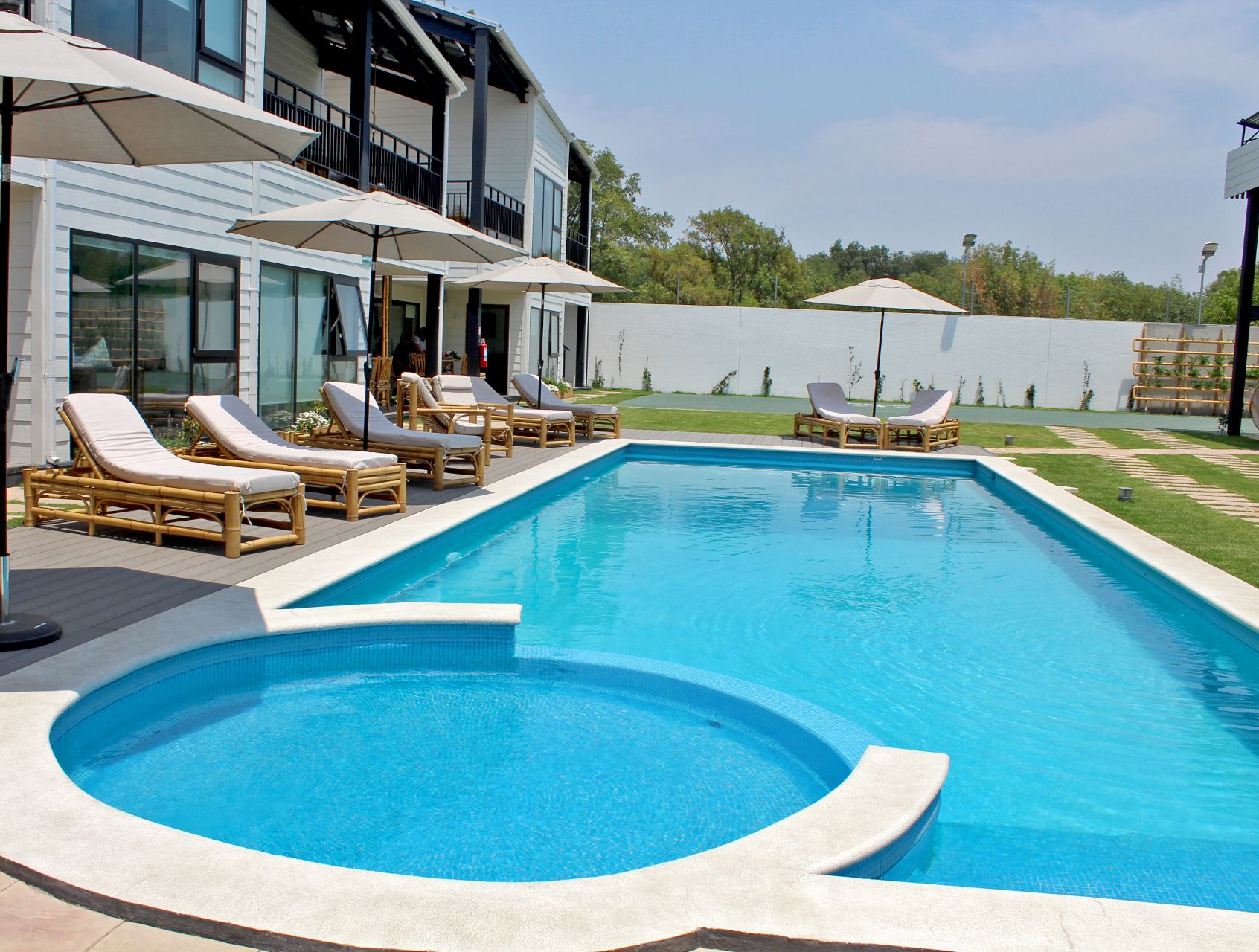 A swimming pool with lounge chairs and umbrellas, surrounded by a modern building with large windows.