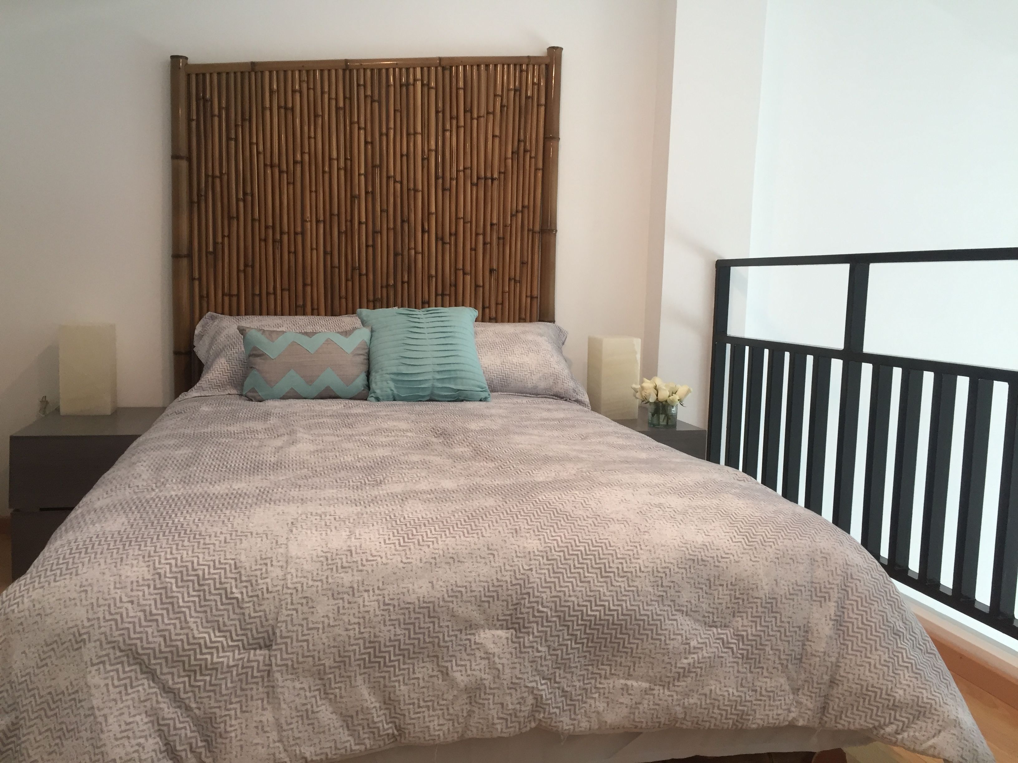 Un lit avec une couvre-lit à motifs, deux oreillers, une tête de lit décorative, des tables de chevet avec des lampes et une vue sur la balustrade d’un balcon.